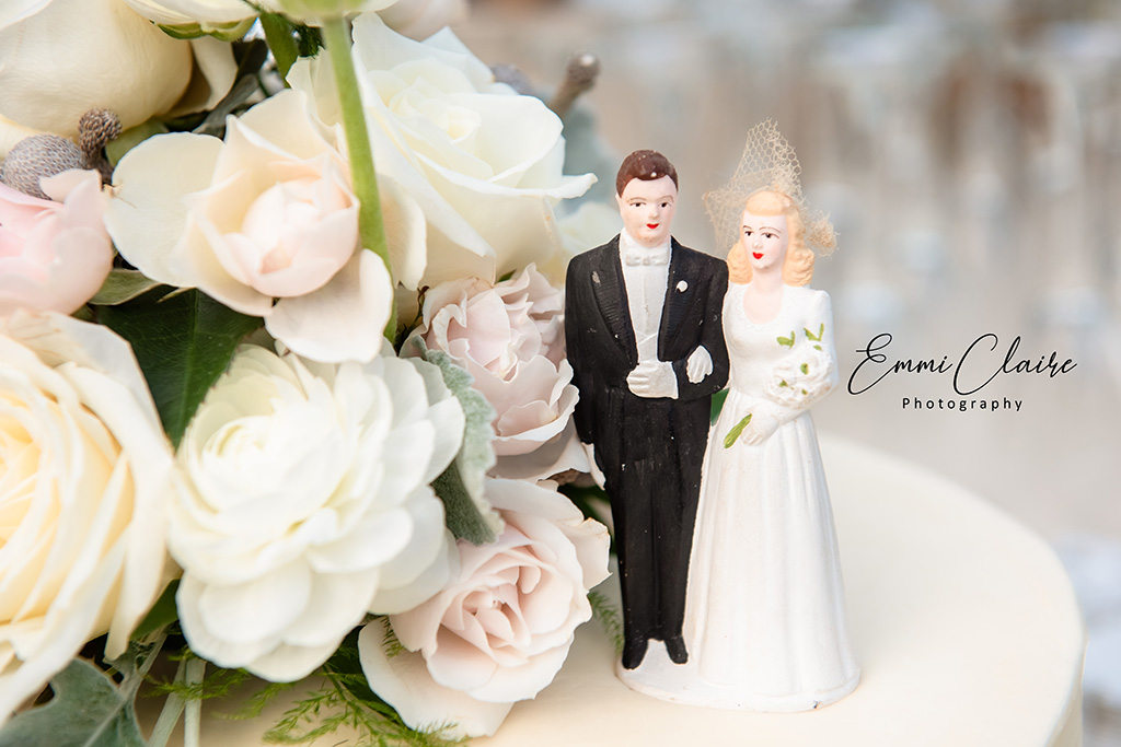 detail shot of a classic bride and groom cake topper on top of a wedding cake beside a bouquet of beautiful nude-colored flowers 