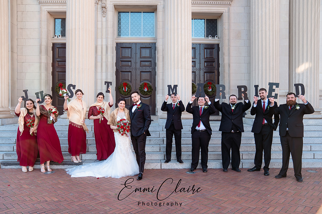 Newlywed couple standing in front of the Cathedral of the Sacred Heart while their bridal party holds up letters behind them that read "Just Married"