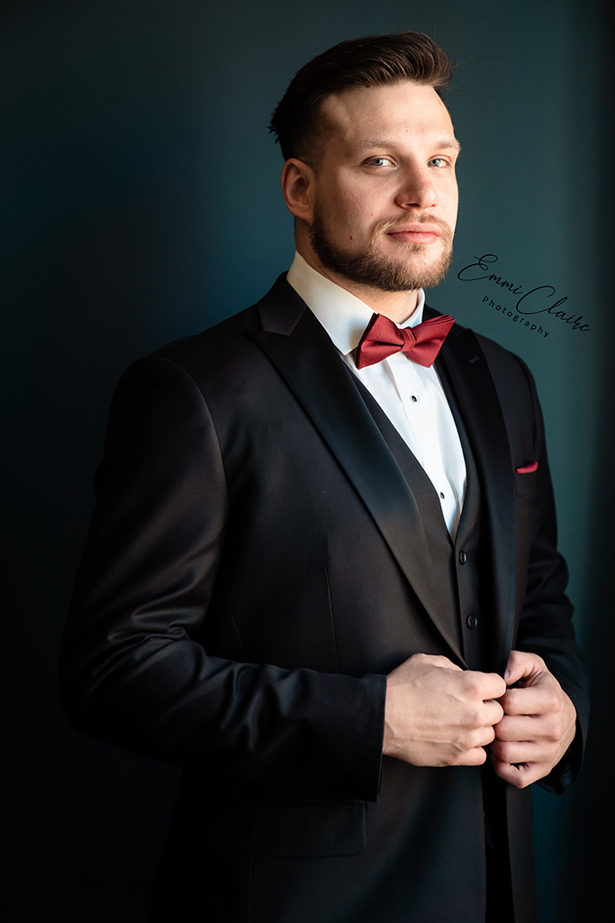 Portrait of the groom standing in his black tuxedo and red bowtie as he prepares to marry his bride in their cathedral wedding