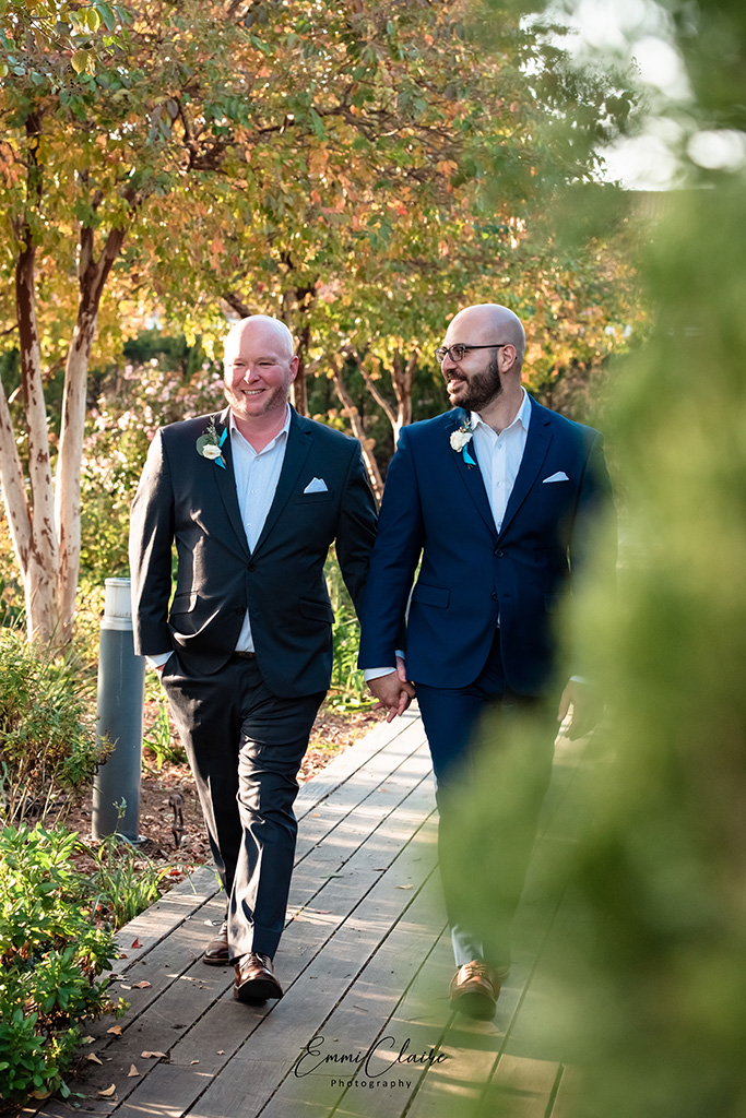 newlywed couple walks hand in hand down a beautiful outdoor path as they celebrate being husband and husband during their COVID wedding