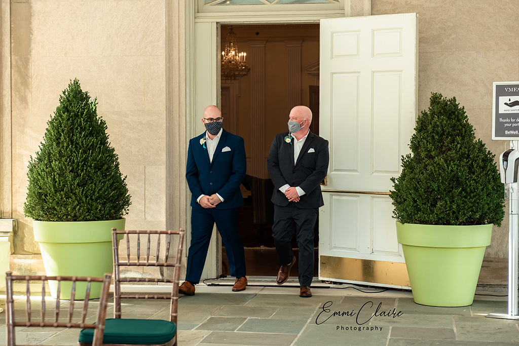 Grooms exiting a door out towards their ceremony area wearing suits and masks to follow the COVID wedding restrictions