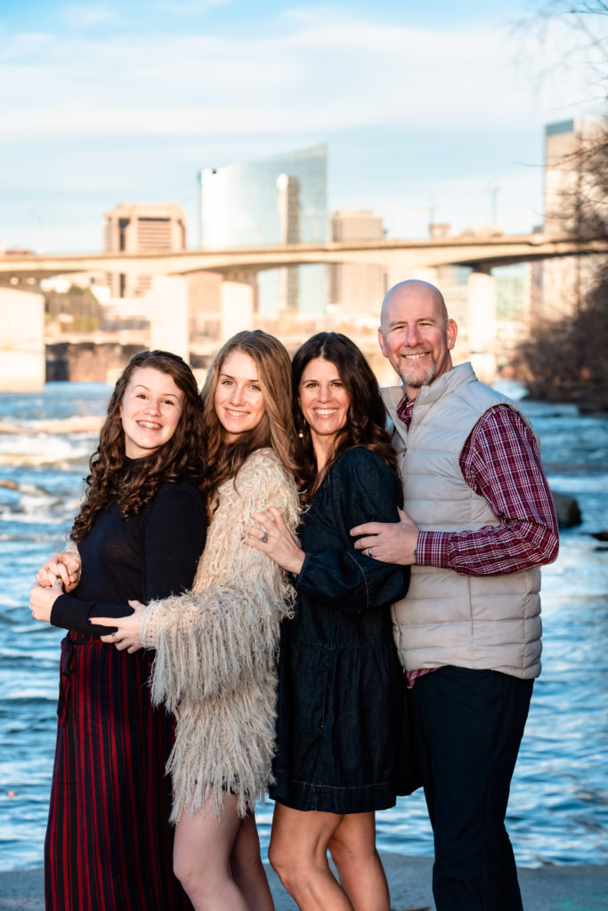 A mother, father, and their two daughters stand together closely to pose for a family photo at Belle Isle