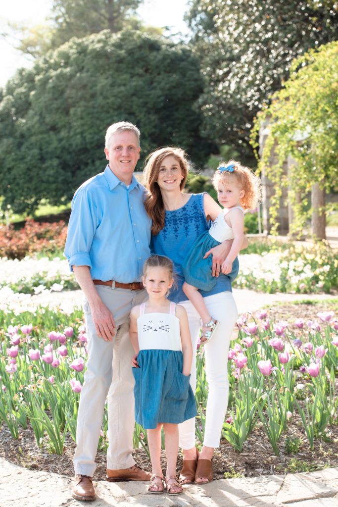 A beautiful couple and their two daughters pose together in the sunlight among beautiful purple tulips that are bloom in the springtime in Richmond 