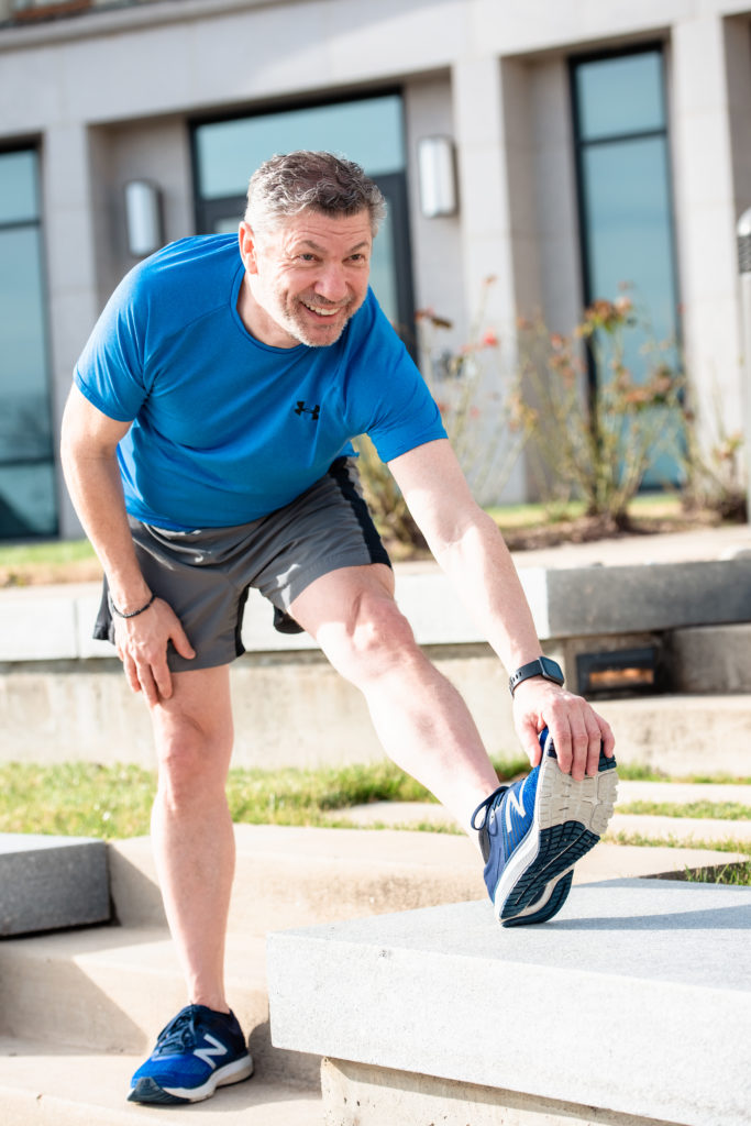 Middle-aged man dressed in workout clothes stretches outdoors during his casual portrait photography session