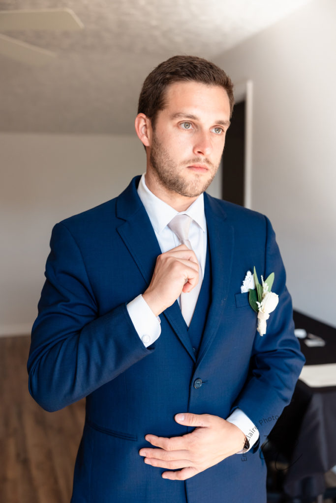 groom straightens his tie and navy blue suit jacket as he prepares for his southern wedding ceremony