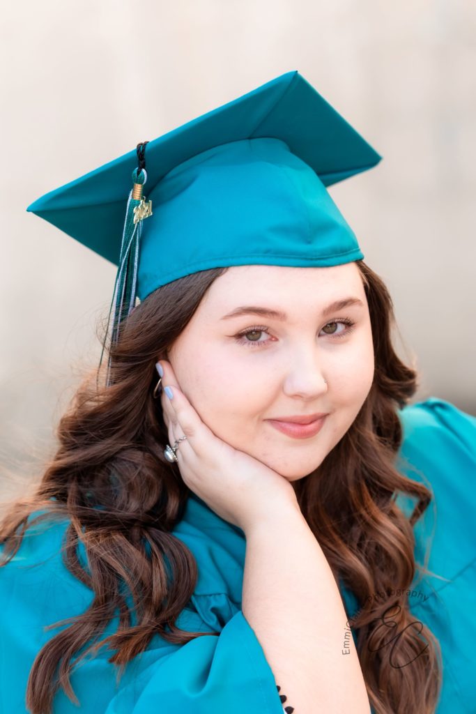 young woman poses with her head resting on her hand for a portrait in her graduation gown and cap for her senior photos