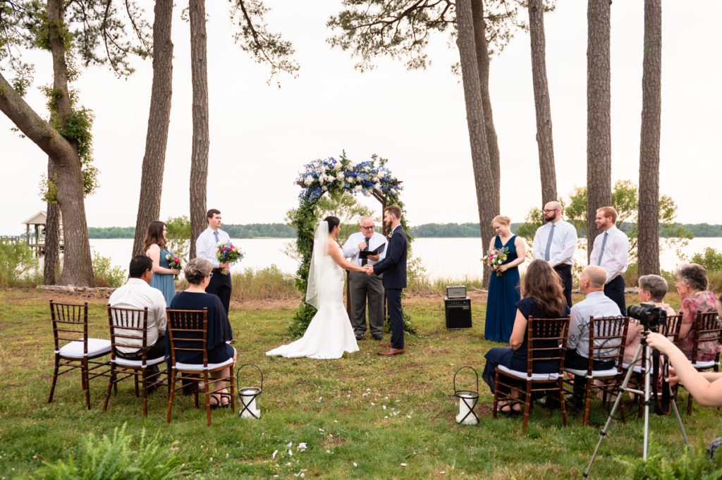 bride and groom stand together in front of an intimate gathering of family and friends as they prepare to be married at their coastal cottage wedding