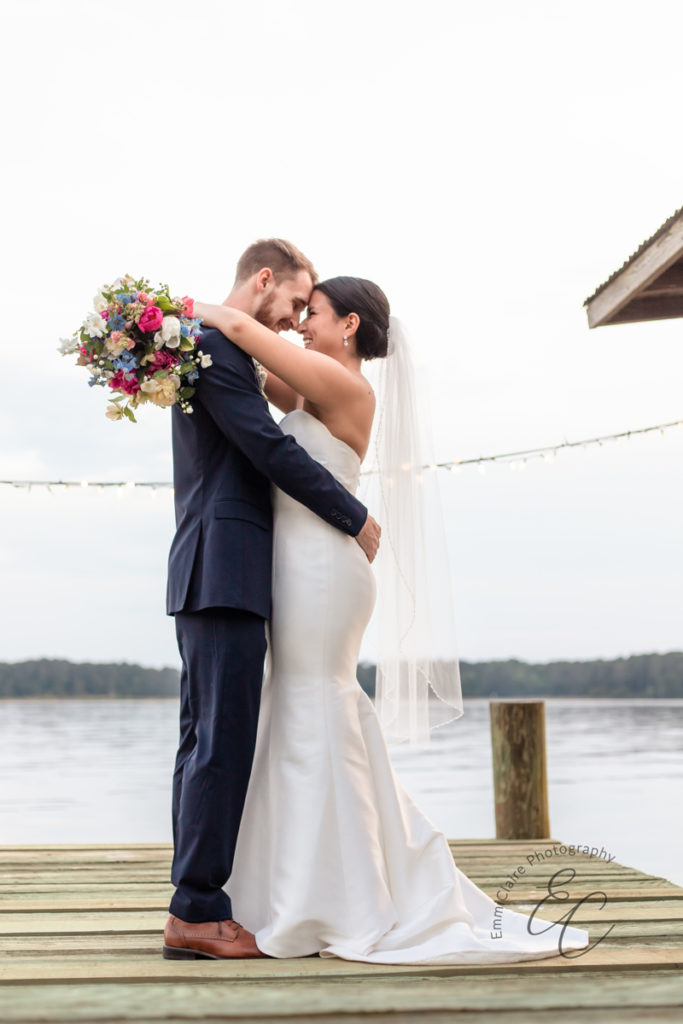 Bride and groom stand out on a dock together during their cottage wedding to share an embrace as they touch foreheads and noses