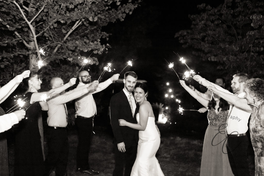 black and white photo of the bride and groom after their reception as their guests surround them with celebratory sparklers to send them off