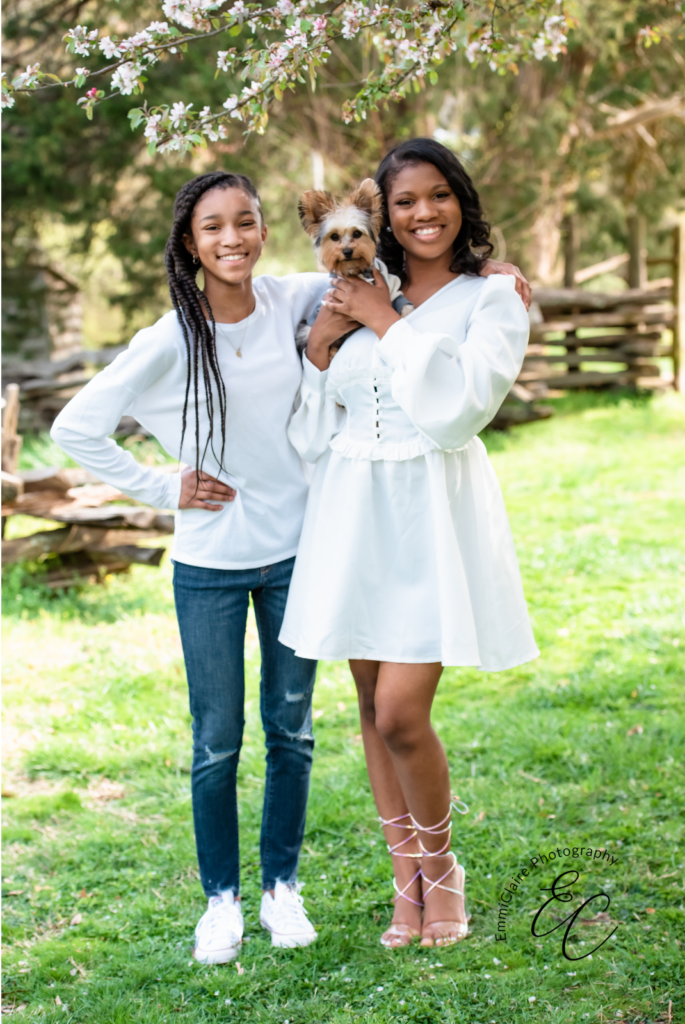 two beautiful young women wearing white tops pose with their dog and smile at the camera exuding confidence