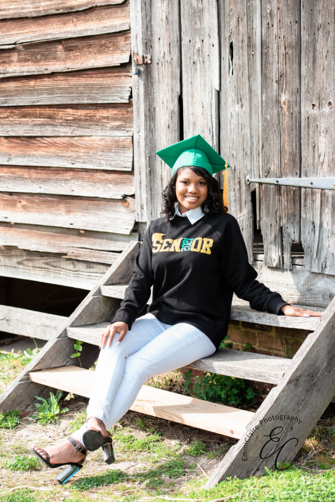 Young woman sitting outside on a wooden staircase in a senior 2021 sweater and her green graduation cap
