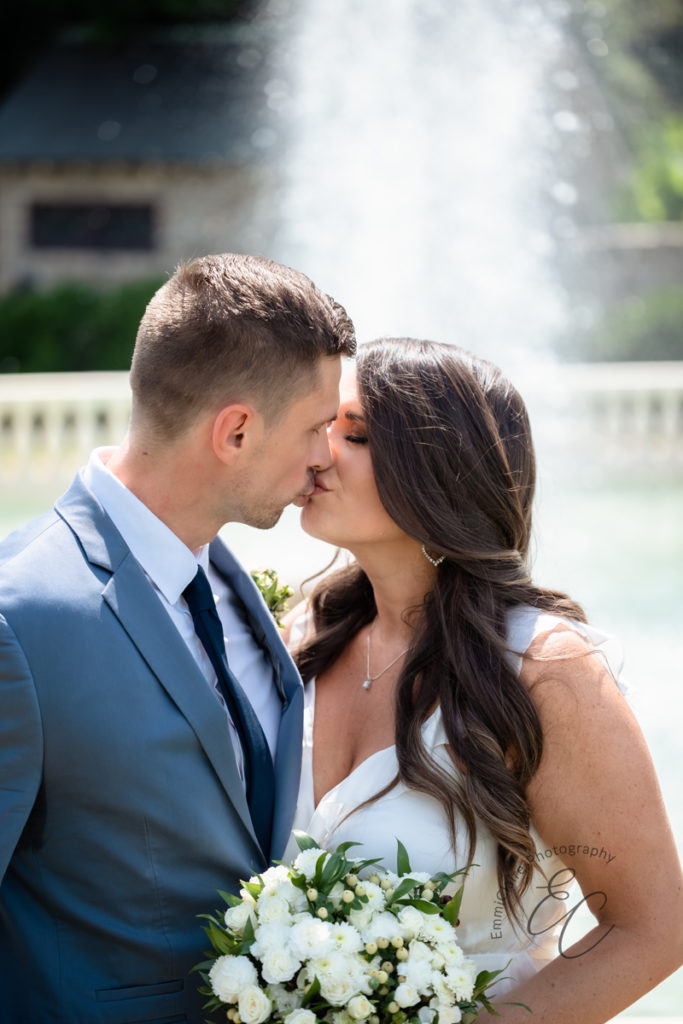 Groom stands in his blue suit while kissing his new wife on the lips after their quaint wedding ceremony