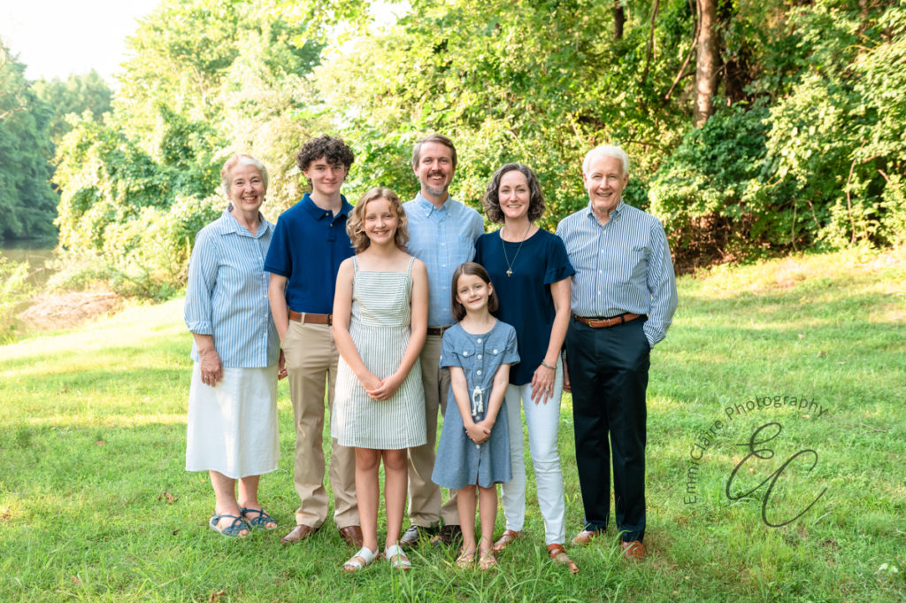 Grandparents, parents, and children stand in the grass together to capture their family together 