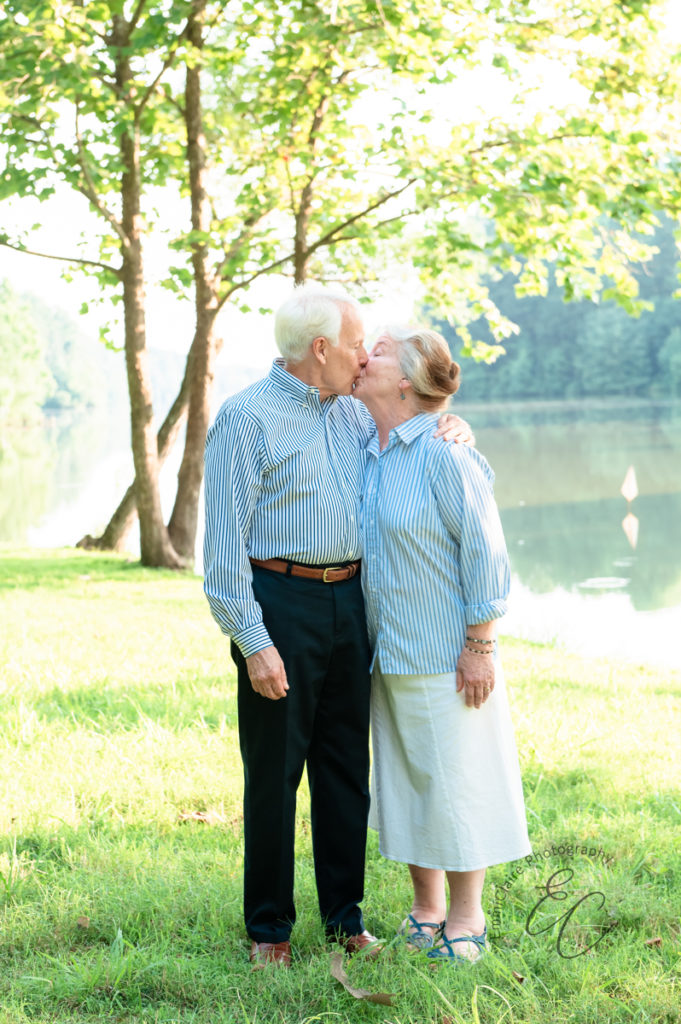 husband and wife in matching white and blue striped shirts share a kiss during an outdoor family photoshoot session