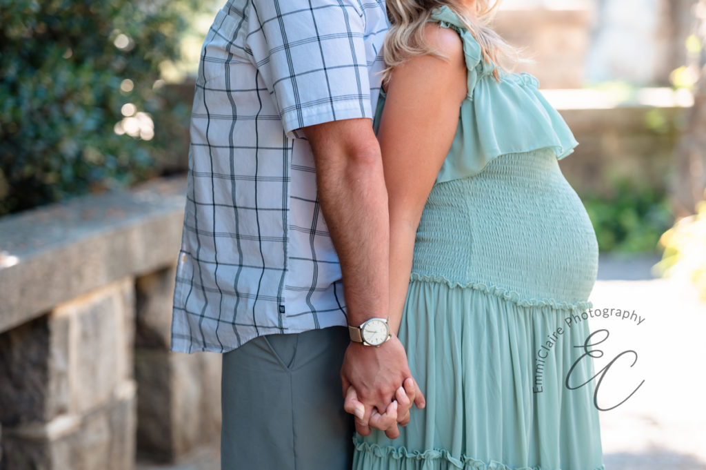 couple standing back to back joins their hands together to pose for their Maymont maternity session