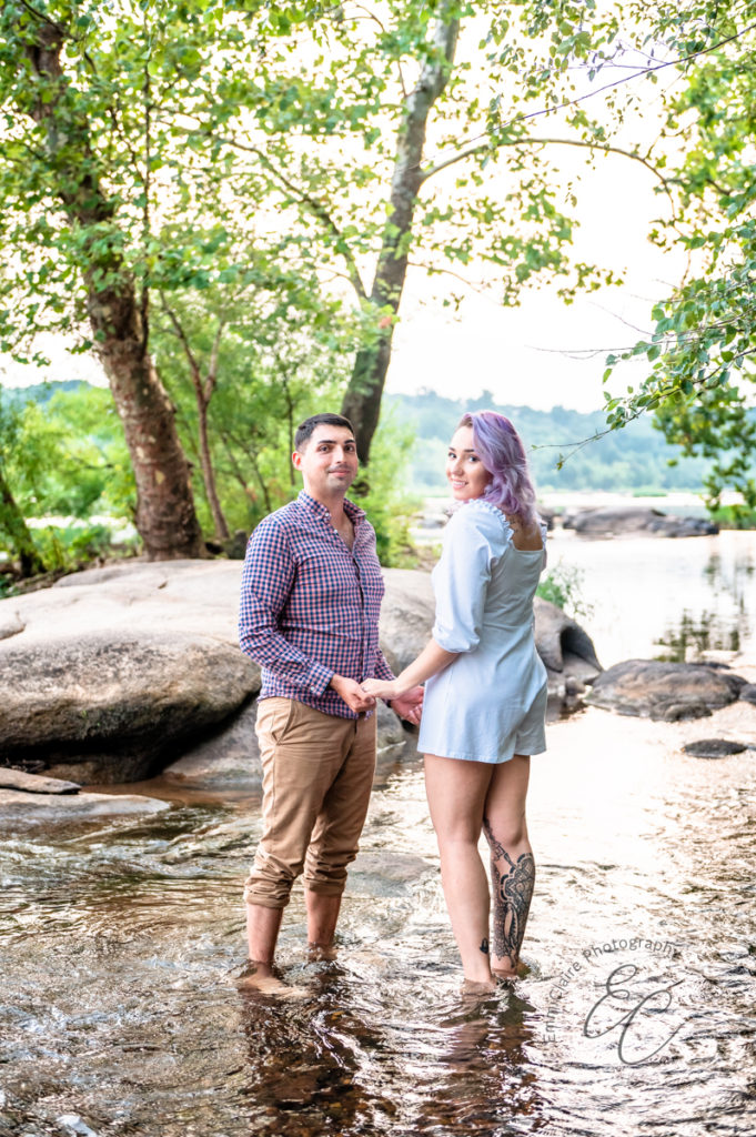 newly engaged couple stands holding hands in a stream together smiling during their outdoor engagement photo session