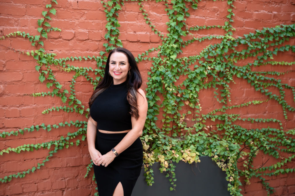 matchmaker poses for her brand photos in front of a red brick wall lined with beautiful green vines