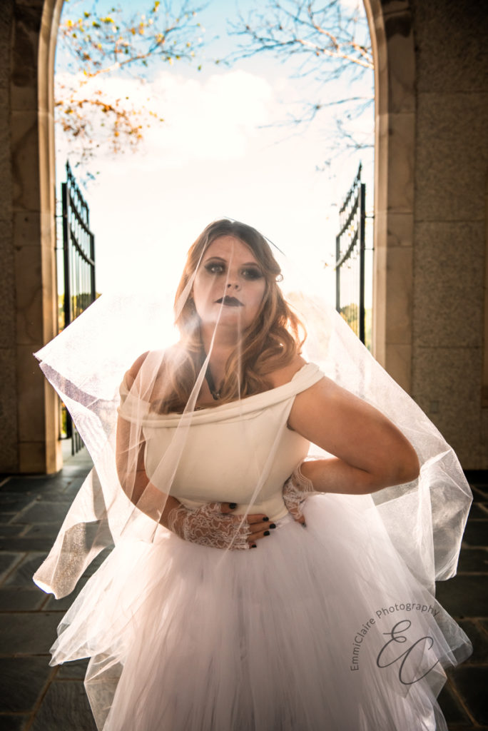 bride stands inside a church in front of the entrance in black lipstick with a veil over her face for a Halloween inspired wedding photoshoot