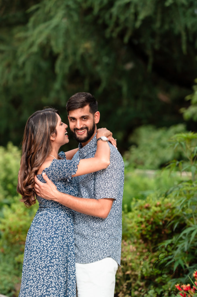 Newly engaged couple laughs and smiles as they hold one another in a beautiful outdoor green space