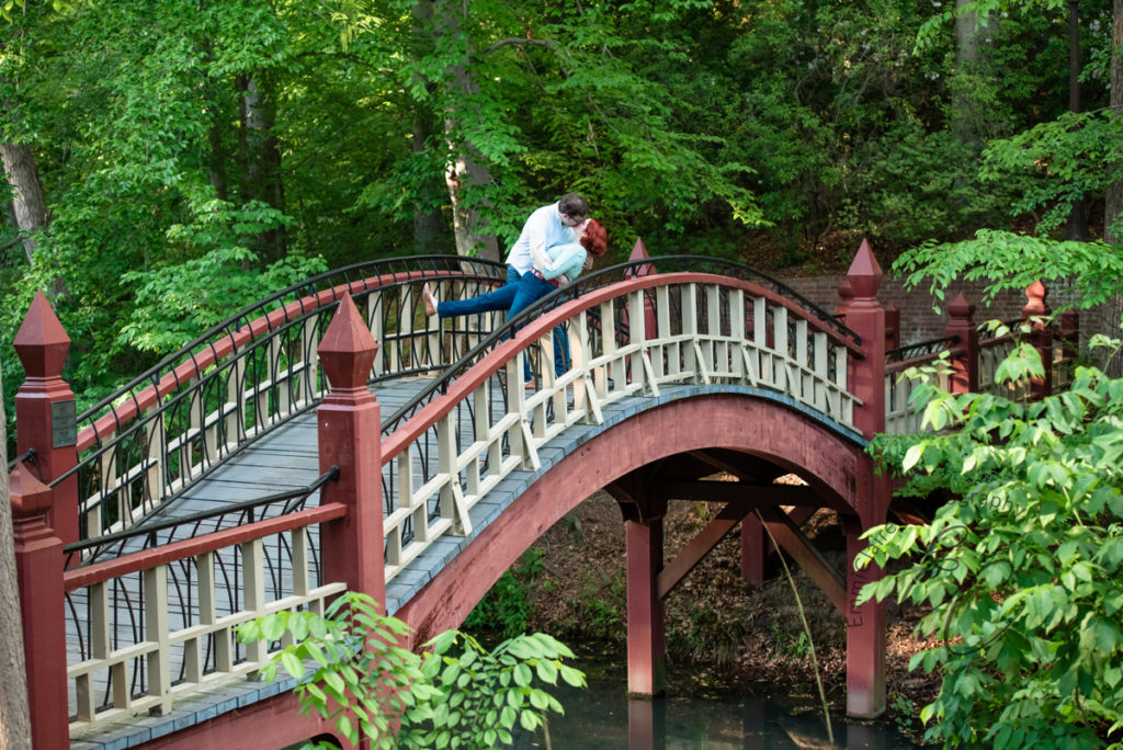 man dips his fiance as they stand in the middle of a beautiful bridge at The College of William & Mary among large green trees