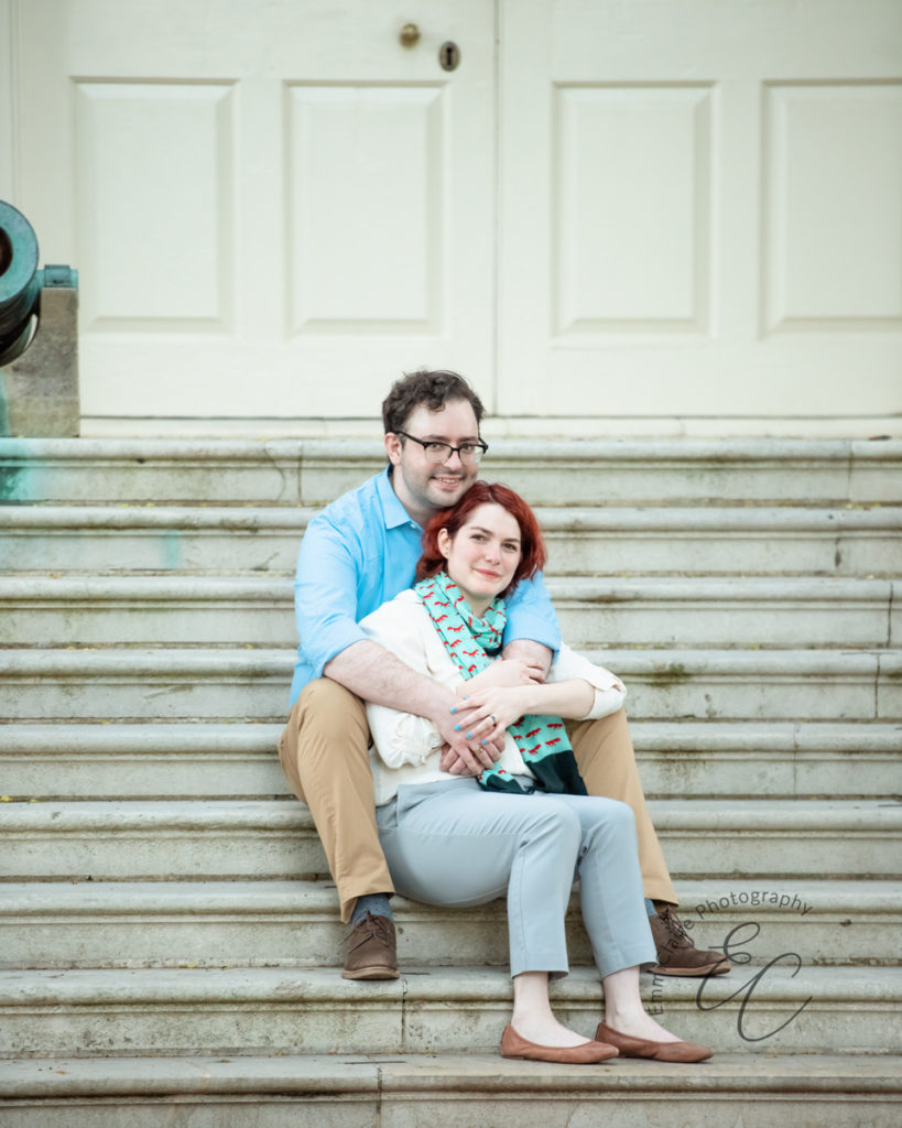 Couple sits together on a white marble staircase to capture and celebrate their engagement