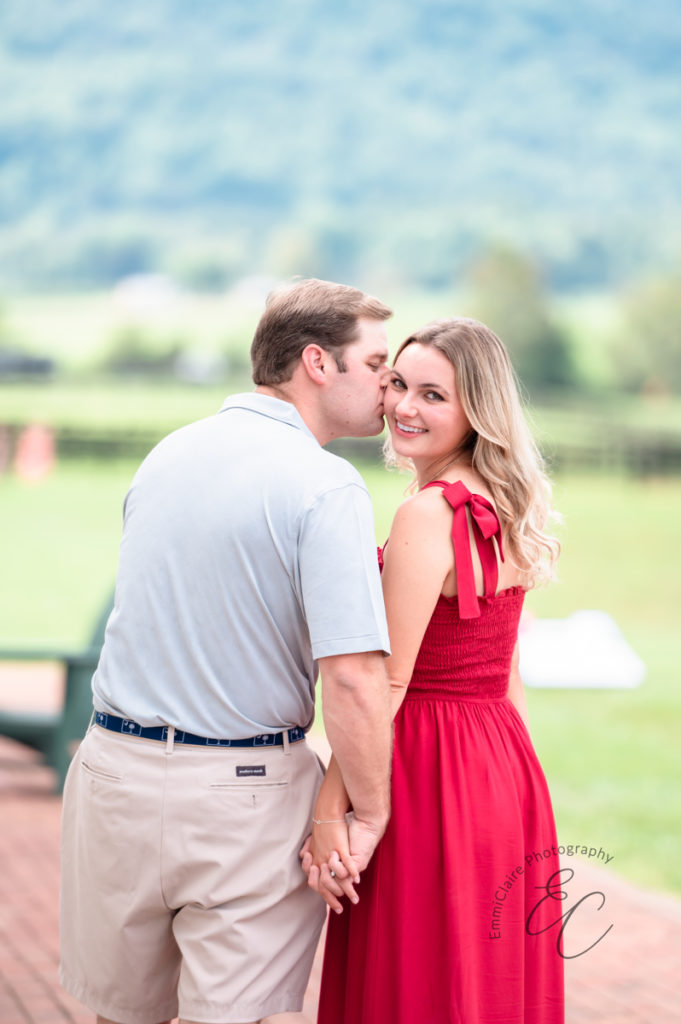 man who just proposed to his girlfriend walks away with her hand in hand and kisses her cheek as the photographer captures their beautiful proposal story
