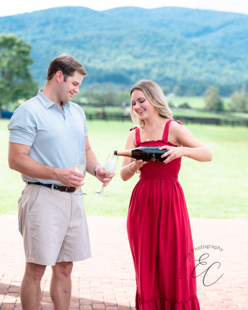 woman in a red dress pours champagne into two glasses her new fiance is holding to celebrate their engagement