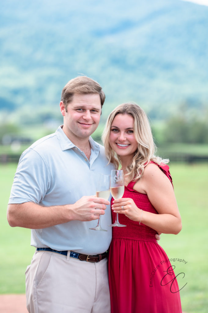 newly engaged couple does a cheers with their champagne glasses to celebrate their engagement in a beautiful green space