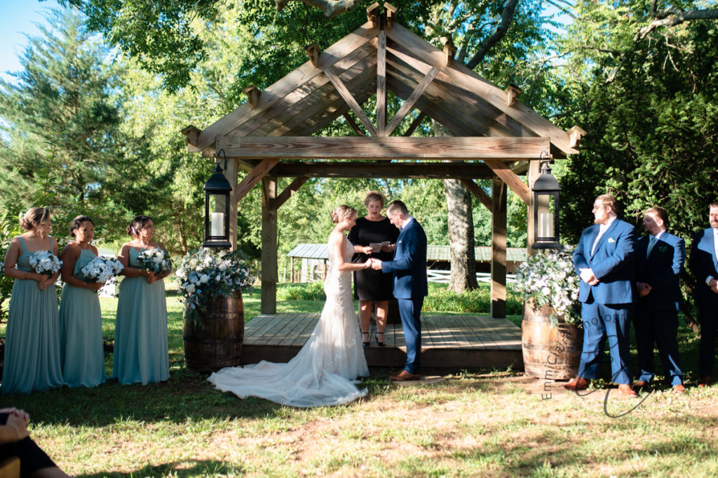 bride and groom stand facing one another in the sun during their outdoor ceremony at Poplar Hill prepared to say "I do" and live happily ever after
