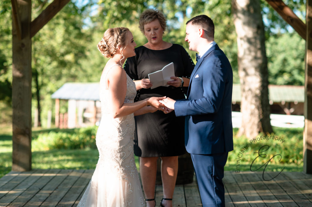bride and groom standing in the sun outside facing one another looking lovingly into one another's eyes as they say "I do" at their pastoral-style wedding