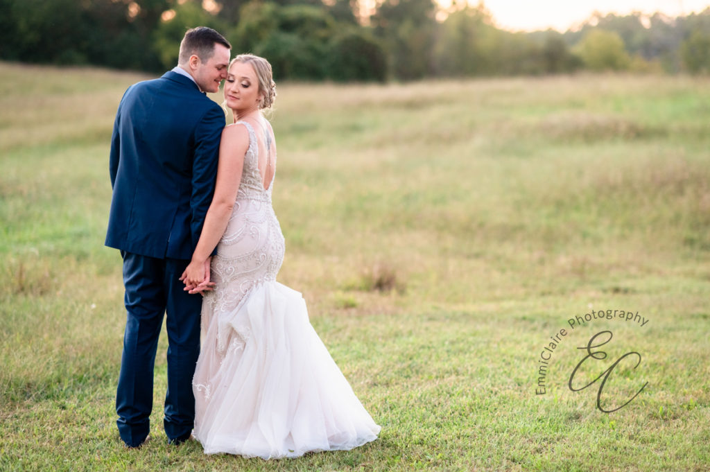 groom and bride walking way from the camera in an open field at their Poplar Hill wedding venue as the groom touches his nose to his wife's cheek who is looking back at the camera