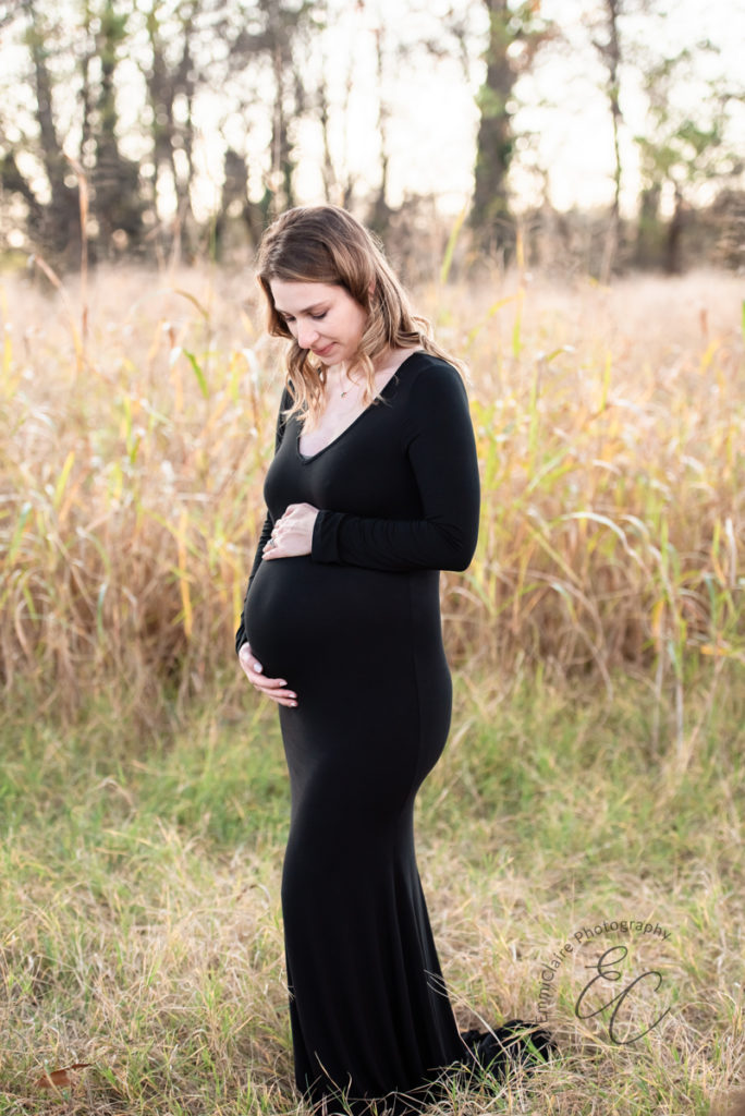 outdoor maternity portrait of an expectant mother in a stunning long, black dress as she looks down at her growing belly
