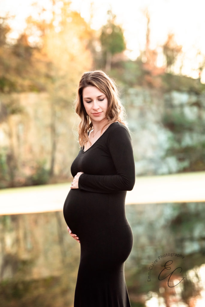 Mother to be in a long black dress lovingly puts one hand above and another hand below her pregnant belly during her outdoor maternity session