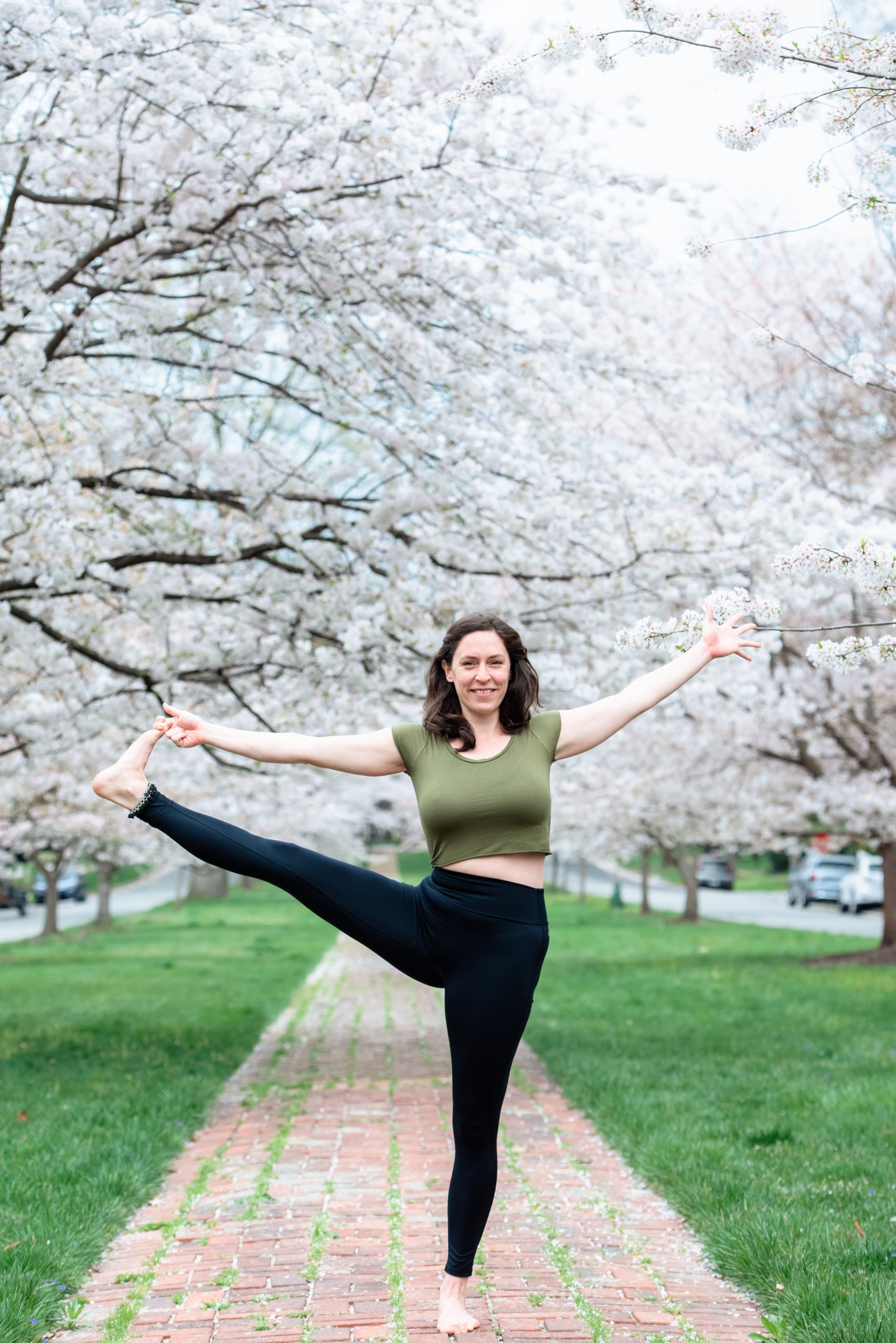 Corinne, Yogi extraordinaire, mediates with her eyes closed in a yoga position under a sea of pale pink cherry blossoms during her Richmond Spring Mini Session with EmmiClaire Photography.
