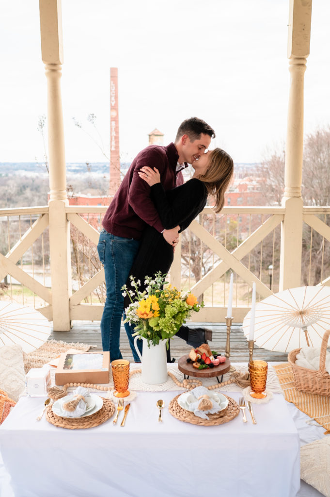 Justin and Caroline kiss under the gazebo with their picnic in the foreground and the Lucky Strike building in the background.