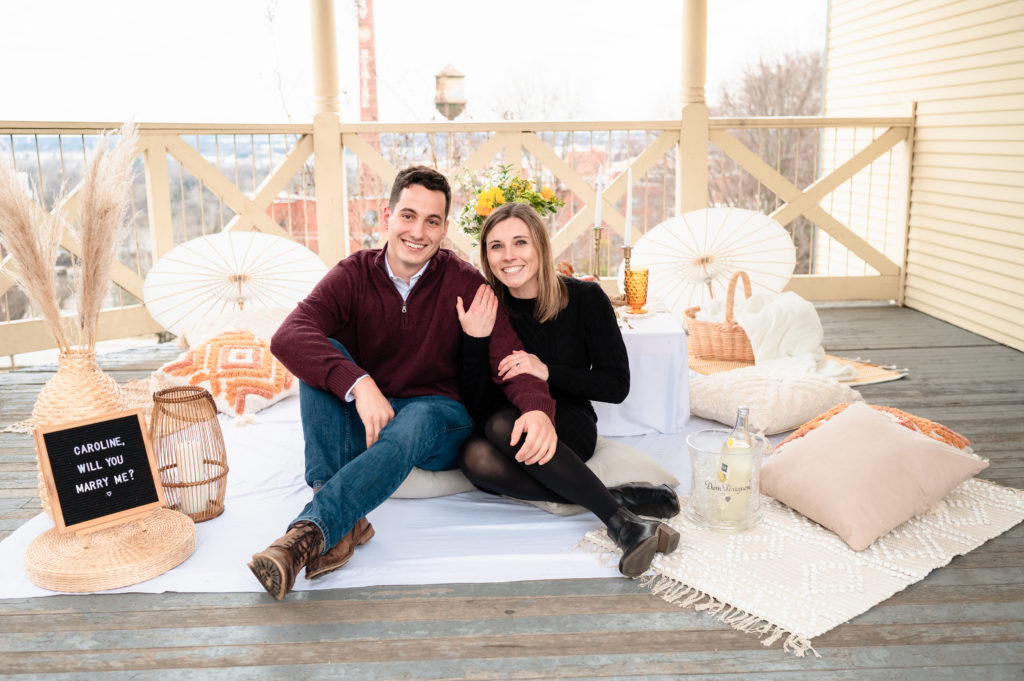 Justin and Caroline sit cuddled up under the gazebo immediately following their proposal at Libby Hill. Behind them, a luxury picnic experience. by RVA Picnics They gaze smilingly at the camera.