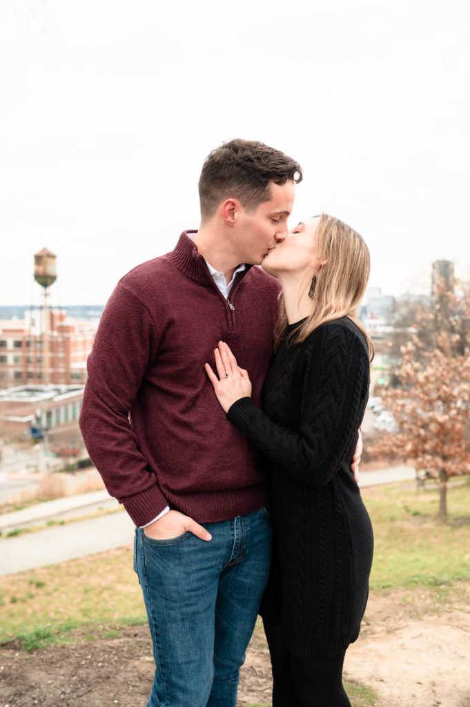 Caroline's hand is on Justin's chest as they kiss at Libby Hill Park with historic Richmond in the background.