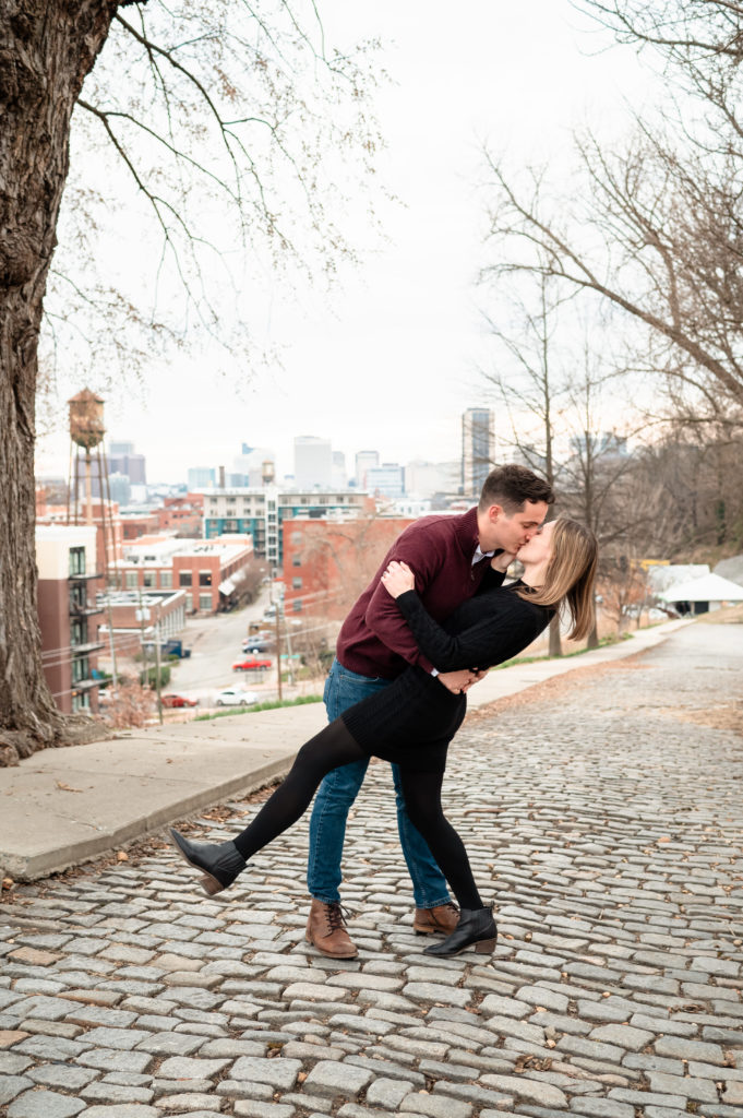 Justin dips Caroline as they kiss on the stone lined streets of Libby Hill Park with the Lucky Strike building in the background. 