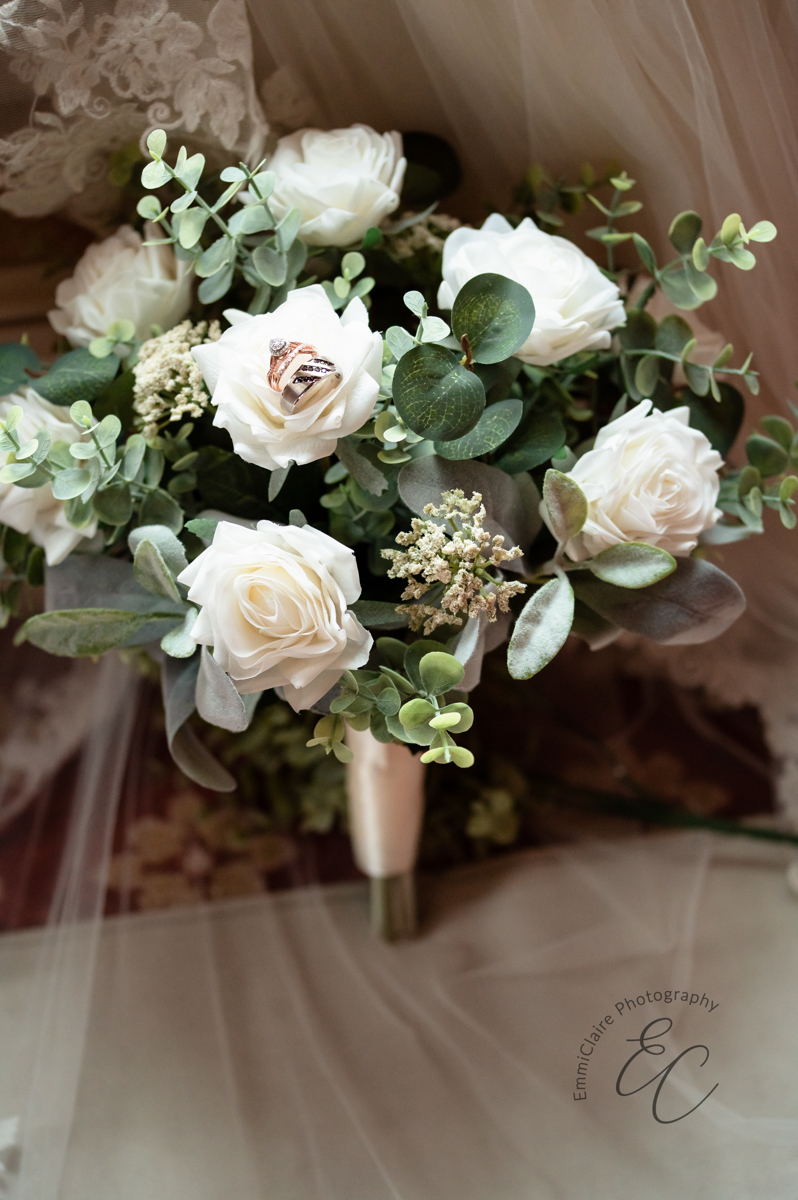 A shot of the bridal bouquet with wedding rings placed in one of the white roses.