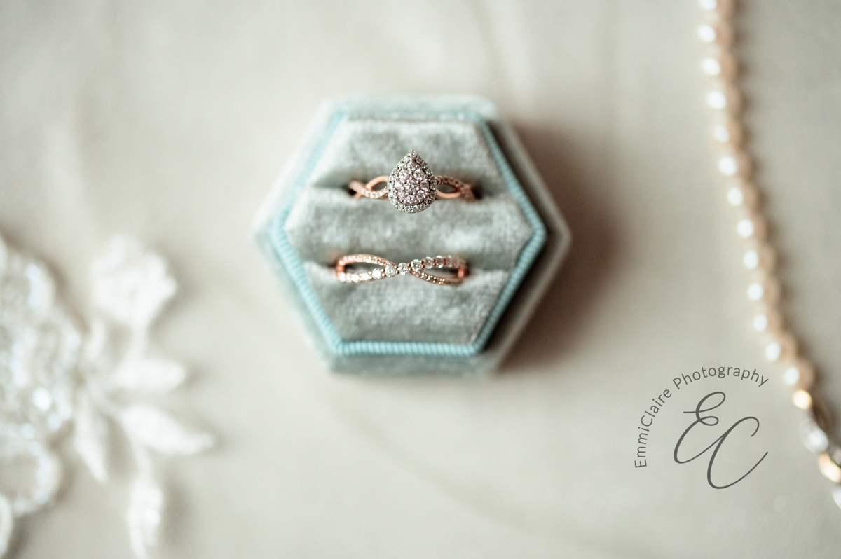 A close up shot of the bride's rings in a sage hexagon ring box with lace veil and pearl necklace the background.