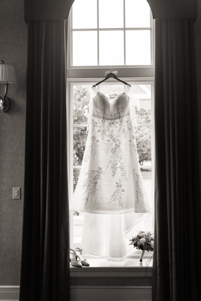 A black and white photo of the bride's dress hanging in a window.