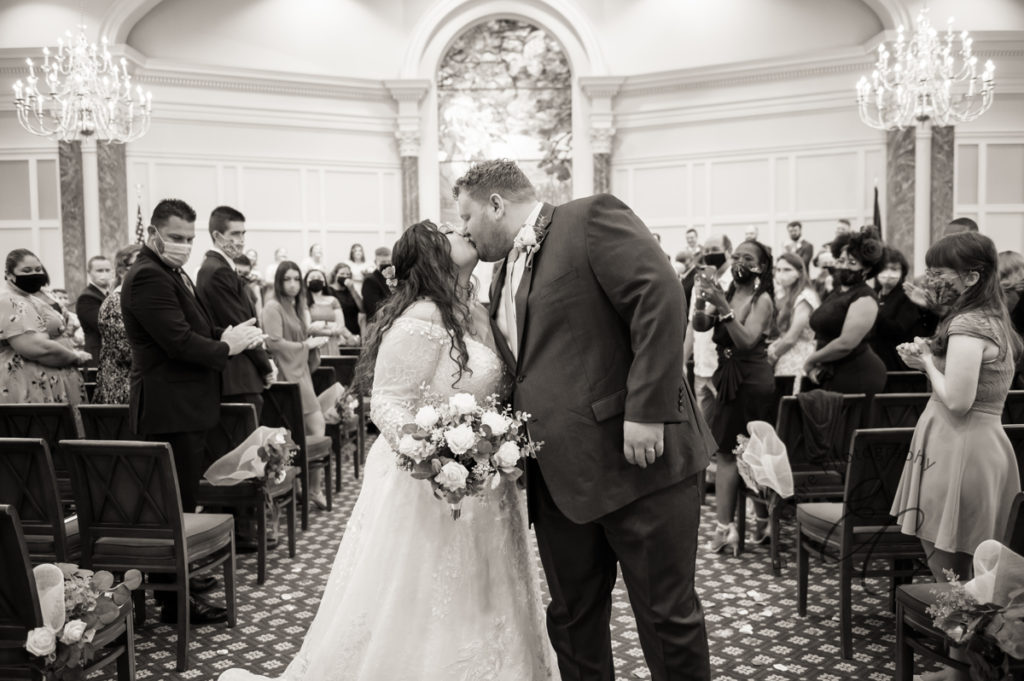 A black and white photo of the bride and groom kiss on their way out of their ceremony at Pope Chapel in Newport News, VA.