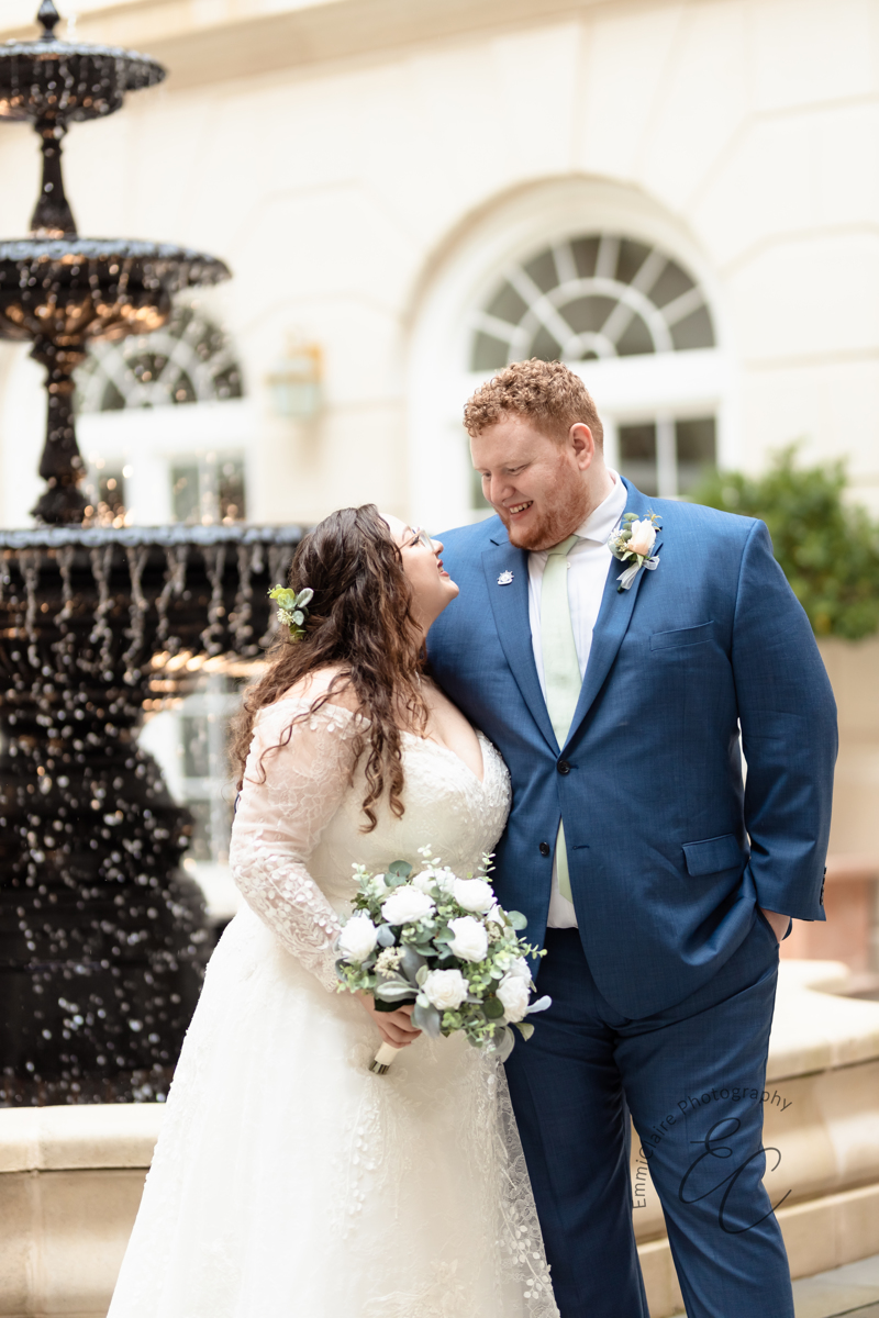 The bride and groom gaze at each other lovingly while standing in front of a beautiful fountain.