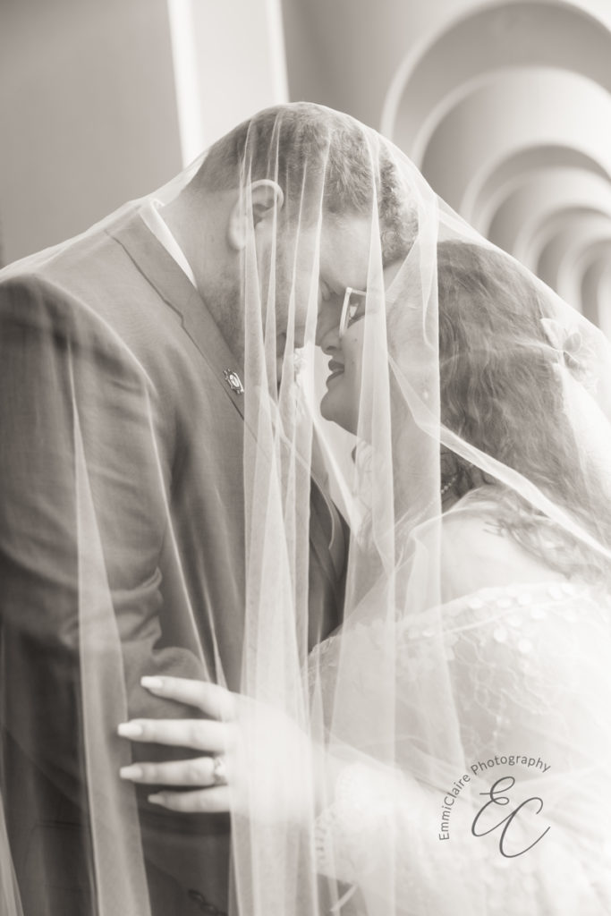 The bride and groom are forehead to forehead with their eyes closed under the bride's veil.