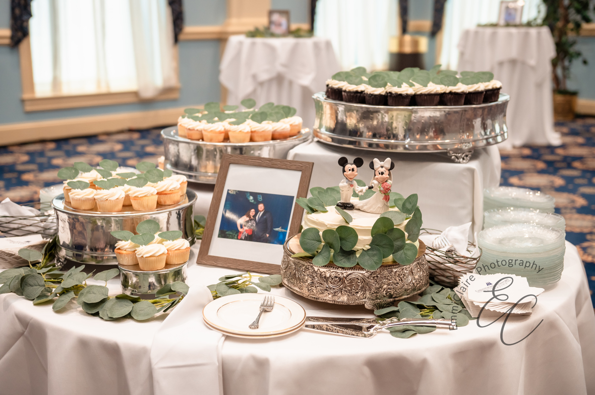 The dessert table - silver cake holders containing a simple white ruffled cake, cupcakes in varying flavors, all adorned with eucalyptus greenery.