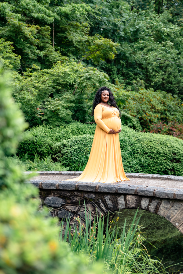 Shana stands on a stone footbridge during her maternity session.