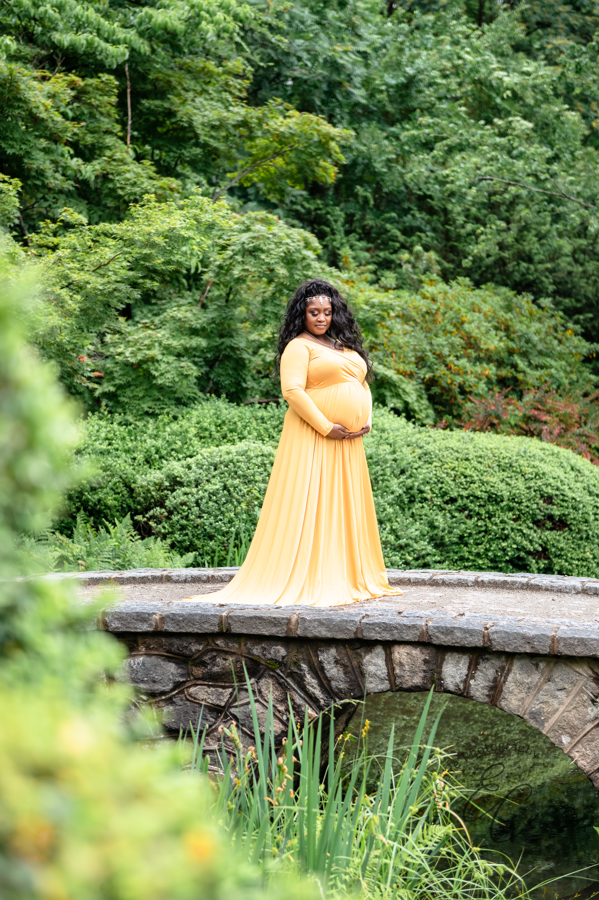 Shana stands on a stone footbridge while gazing down at her belly during her maternity session.