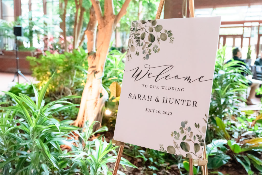 Sign reading "Welcome to our wedding Sarah & Hunter July 10, 2022" greets guests as they arrive at the atrium wedding ceremony