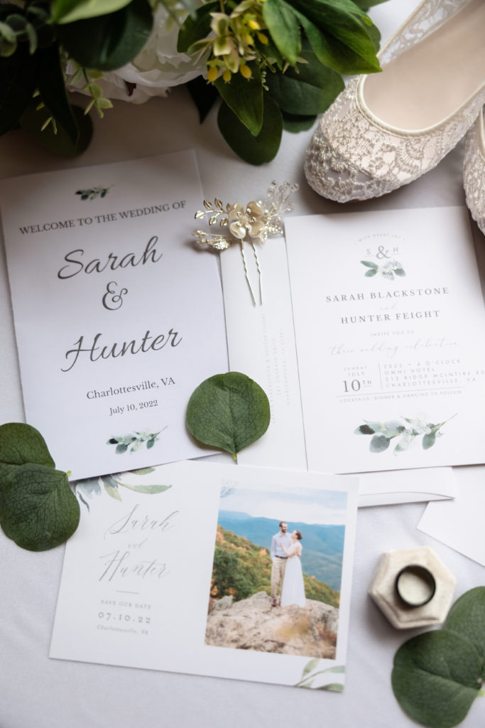 Flatly of wedding invitation, save the ate, and program with eucalyptus leaves, wedding band, and bride's accessories (shoes and hair pin)