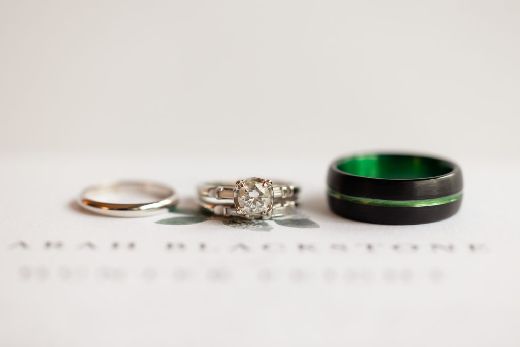 wedding bands and engagement ring rest on top of wedding invitation